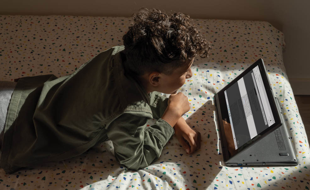 Un joven sigue las clases a través de un ordenador tumbado en una cama