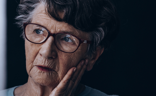 Una mujer mayor que sufre alzhéimer mira por una ventana