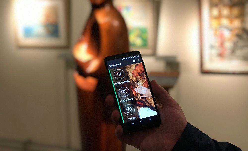 Una mano sujeta un teléfono con la aplicación Amuse frente a una escultura en un museo