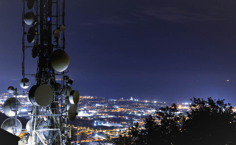 Fotografía de una antena de telefonía móvil a las afueras de una ciudad de noche