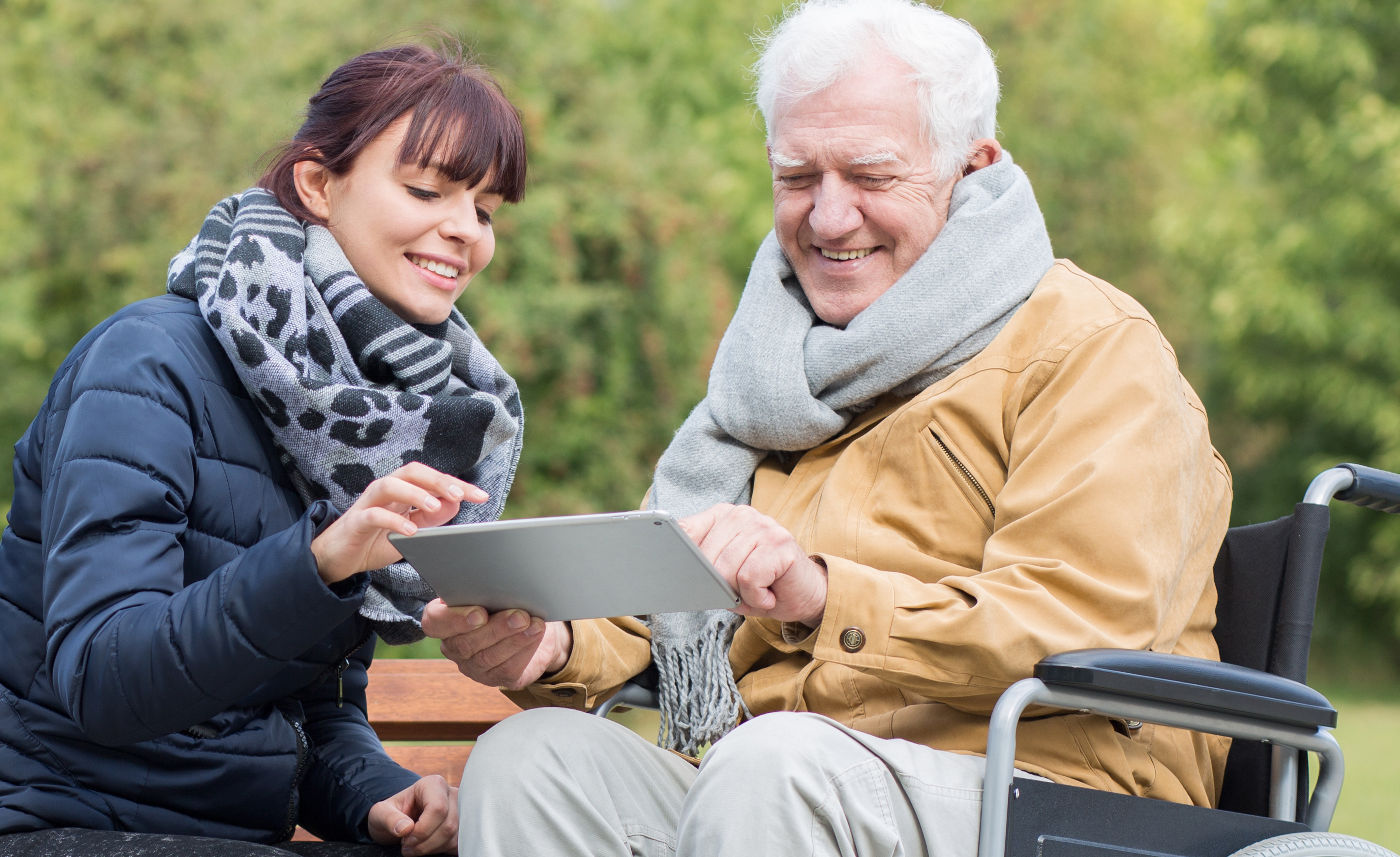 Un hombre en silla de ruedas y una mujer joven miran juntos una tableta en un parque