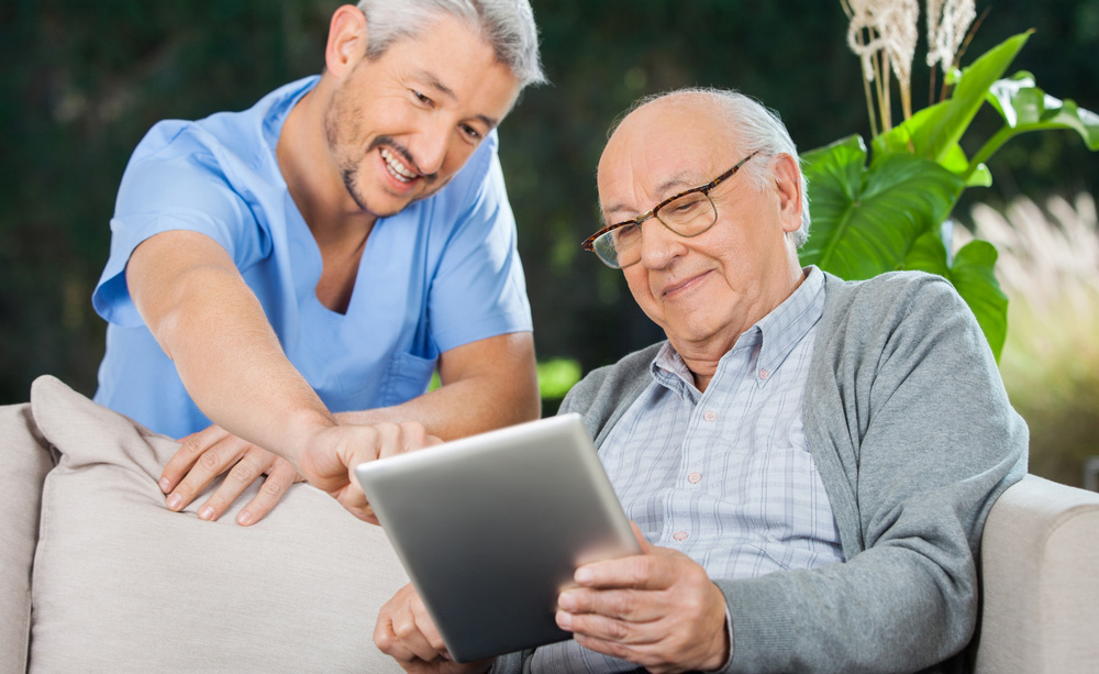 Una persona mayor utiliza una tableta junto a un asistente