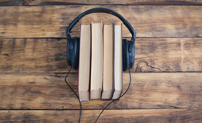 Fotografía de unos libros con unos auriculares alrededor sobre una mesa de madera