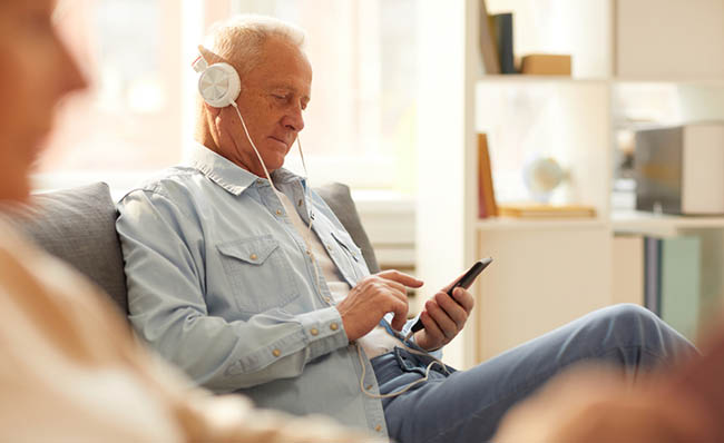 Un hombre mayor escucha un audiolibro desde su teléfono móvil
