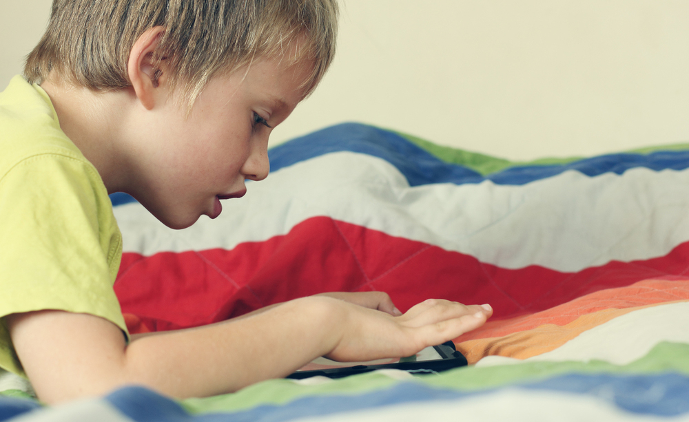Un niño tumbado en una cama utiliza una tableta
