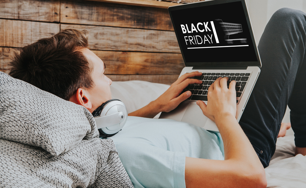 Un joven tumbado en un sof&aacute; compra en el Black Friday con su ordenador