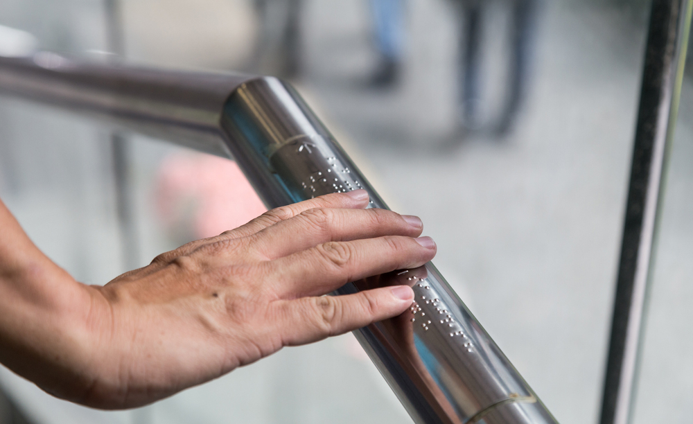 Una persona ciega lee el etiquetado braille sobre una barra de metal