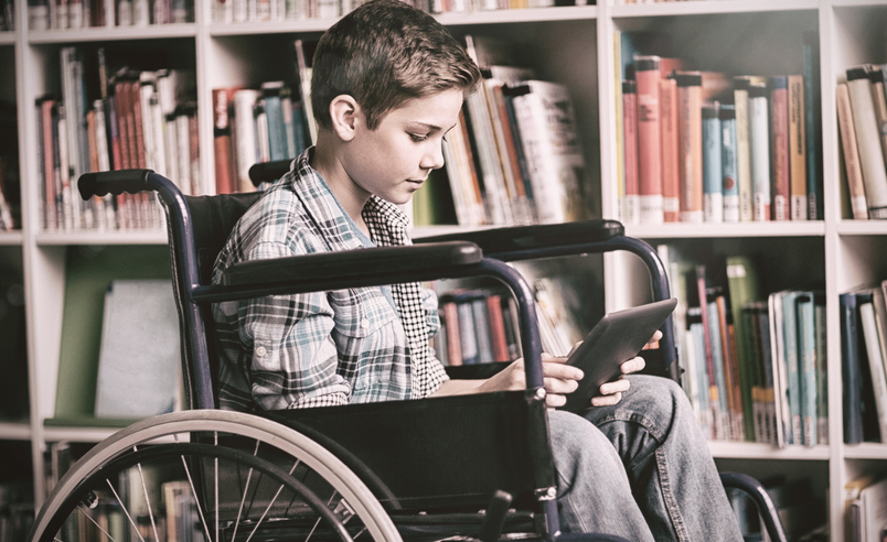 Un joven en silla de ruedas utiliza una tableta en una biblioteca