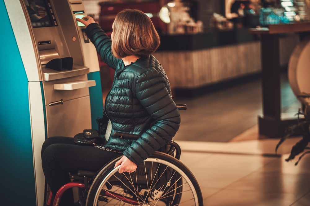 Una mujer en silla de ruedas saca dinero de un cajero