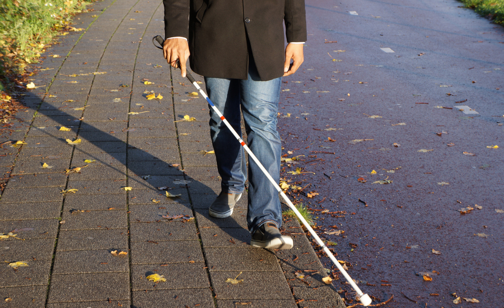 Una persona ciega camina por la acera cerca de un parque
