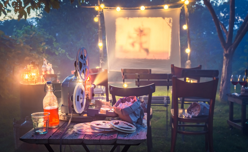 Fotografía de un cine exterior casero, con sillas, un proyector y una tela colgada a modo de pantalla