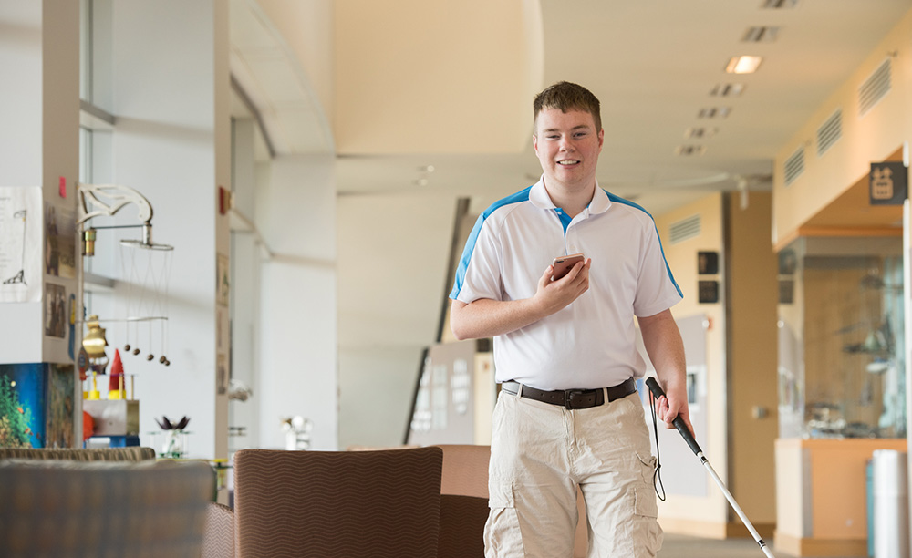 Un joven con discapacidad visual utiliza la app Clew y su bastón para moverse dentro de un edificio
