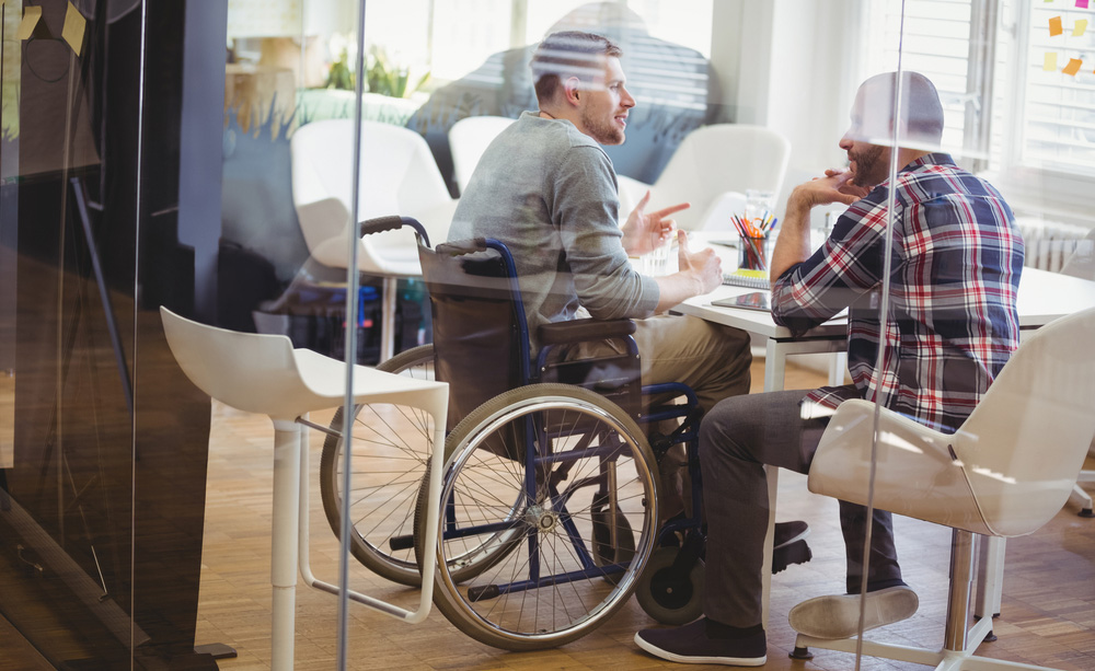 Fotografía de un joven en silla de ruedas en una oficina hablando con un compañero