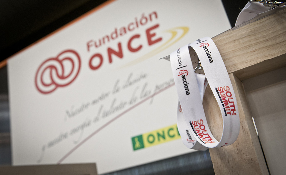 Fotografía de una acreditación para South Summit con un cartel de Fundación ONCE al fondo