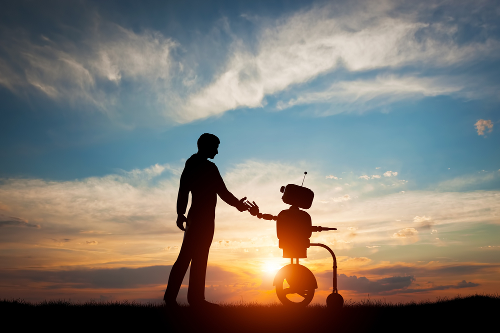 Un robot y un ser humano se dan la mano con un atardecer de fondo