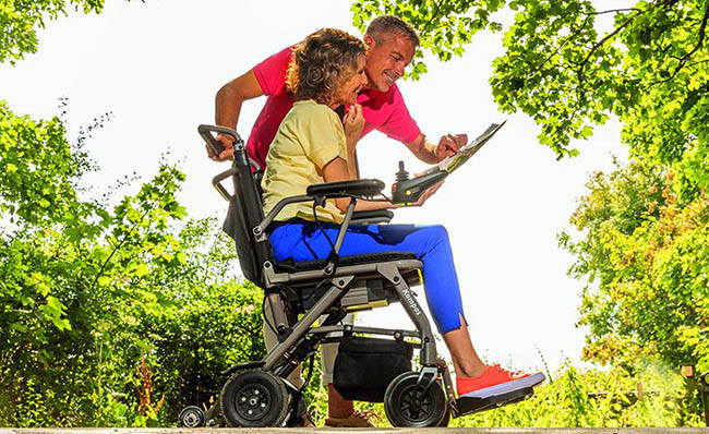 Una mujer utiliza una silla Invacare Kompas mientras mira un mapa junto a otra persona