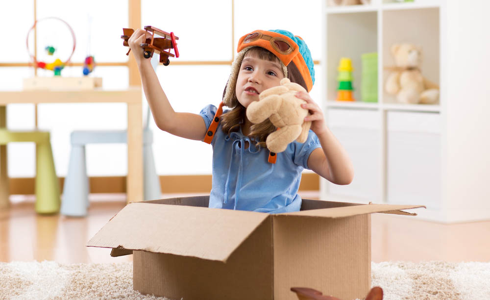 Una niña juega con varios juguetes dentro de una caja de cartón