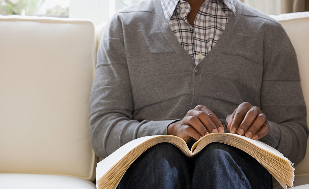 Una persona lee un libro braille sentado en un sofá