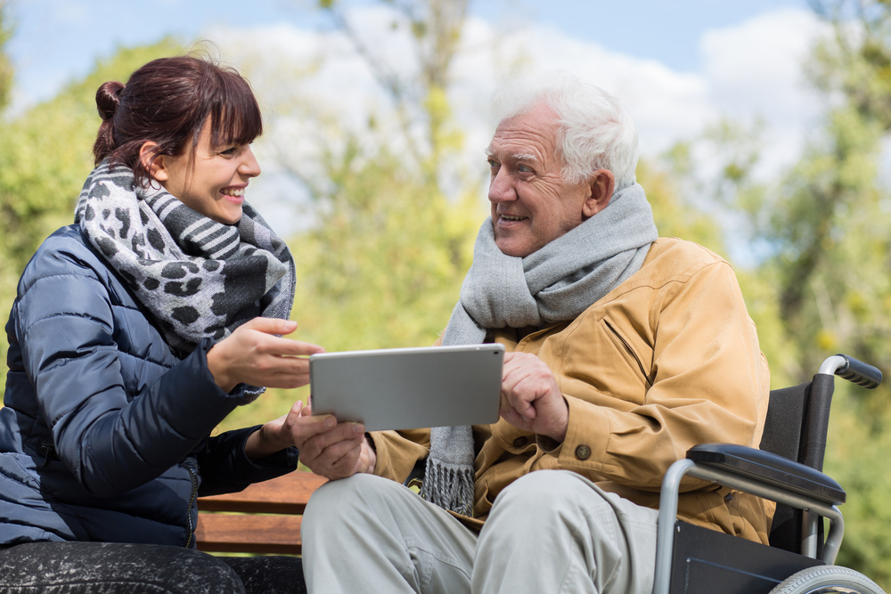 Una personas mayor en silla de ruedas utiliza una tableta junto a una mujer joven
