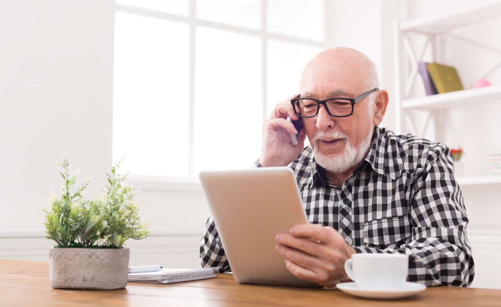 Un hombre mayor utiliza una tableta mientras habla por teléfono