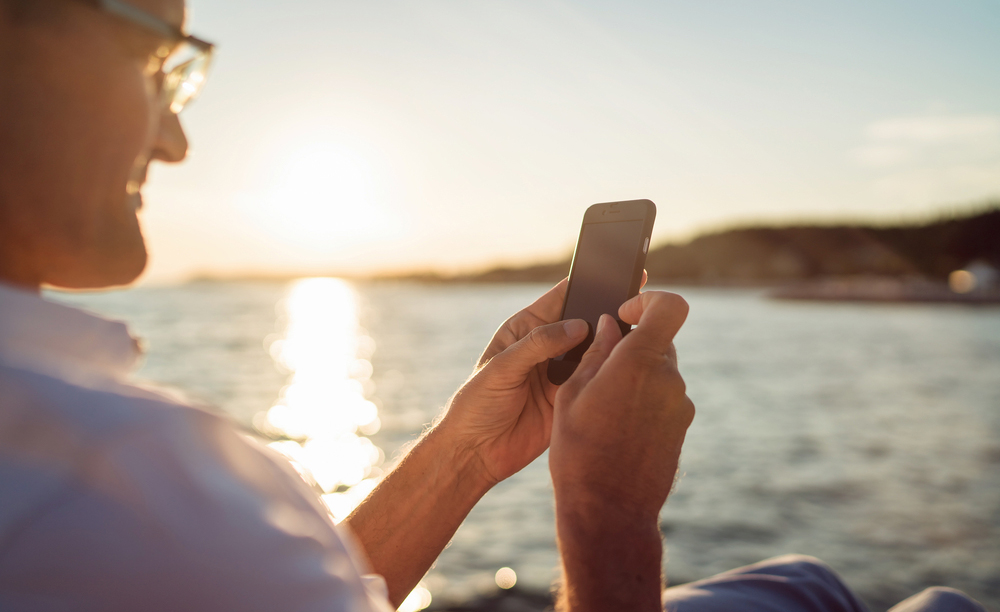 Un hombre utiliza su tel&eacute;fono m&oacute;vil con el mar al fondo