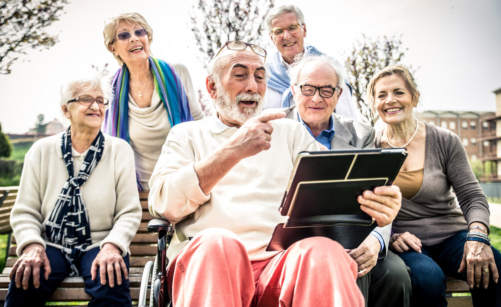 Varias personas mayores utilizan juntas una tableta sentadas en el banco de un parque