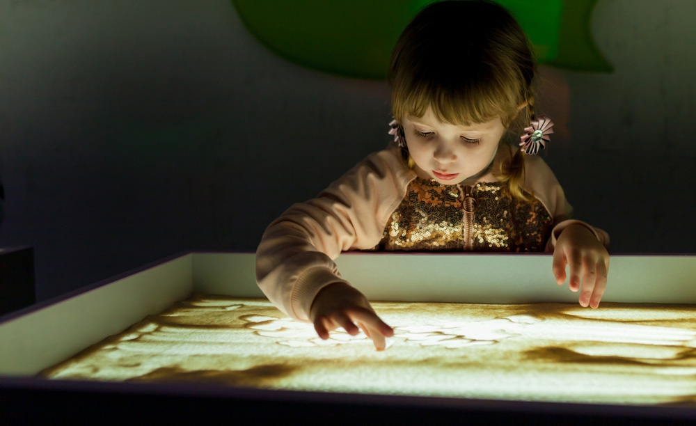 Una niña experimenta con la arena sobre una mesa de luz