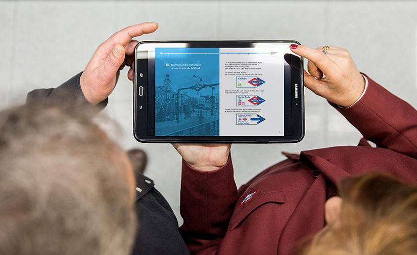 Una empleada de Metro de Madrid ayuda a un usuario a utilizar el suburbano mostrando la guía en lectura fácil en una tableta