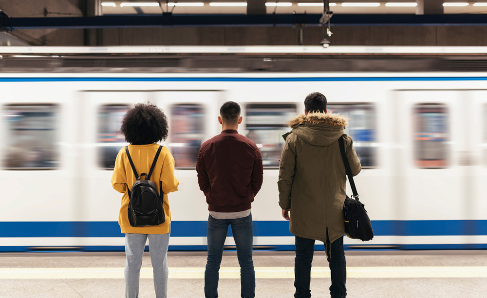 Varios jóvenes esperan en un andén del Metro de Madrid mientras pasa un tren
