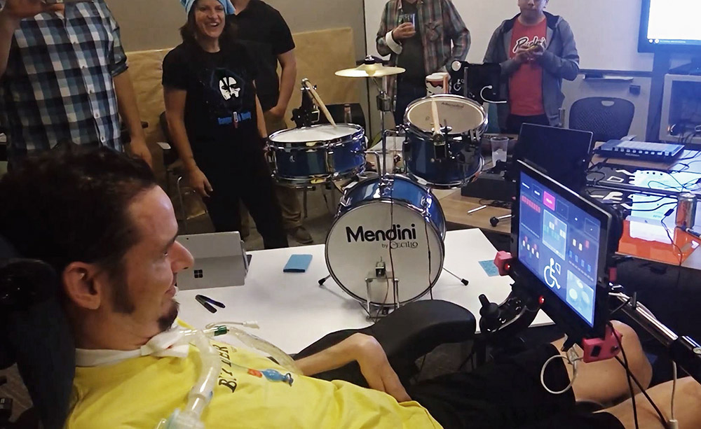 Fotograma de un vídeo de Microsoft que muestra a Jeremy Best utilizando 'Hands-Free Music' para tocar la batería, rodeado de varias personas