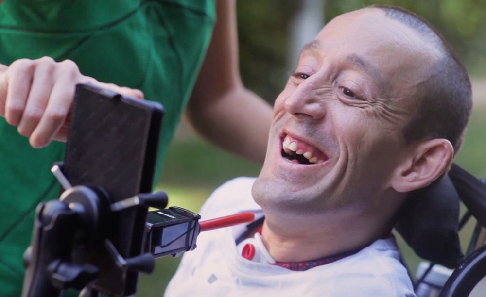 Un hombre con discapacidad física utiliza su smartphone con un pulsador y Mouse4all