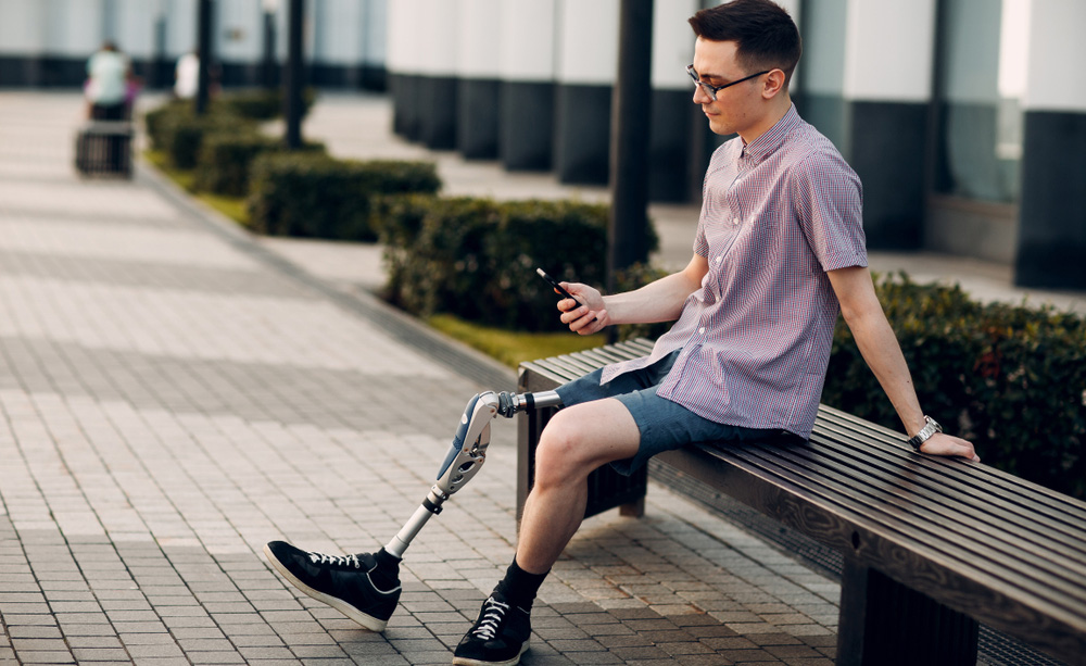 Un joven con pierna ortopédica mira su móvil sentado en un banco en la calle