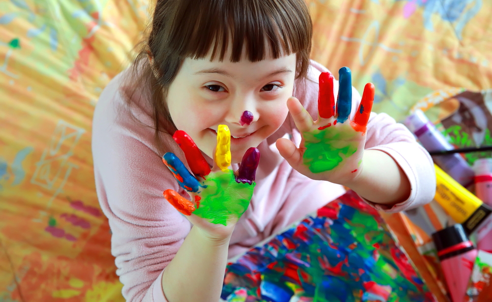 Una niña con síndrome de Down sonríe y juega con las manos pintadas