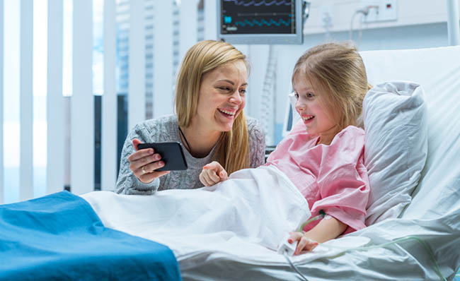Una niña ingresada en un hospital mira un móvil con su madre