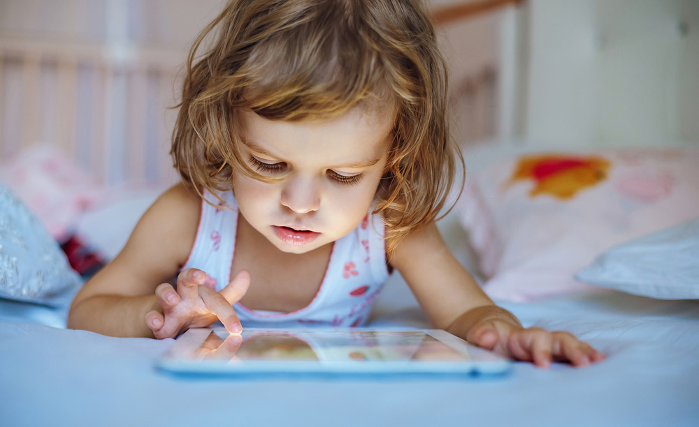 Una ni&ntilde;a utiliza una tableta tumbada en una cama