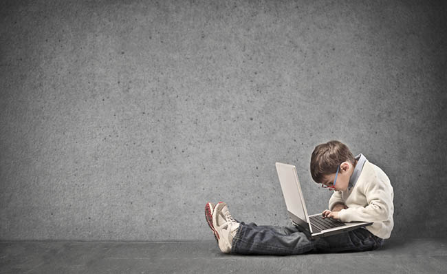 Un niño utiliza un ordenador portátil sentado en el suelo frente a una pared gris