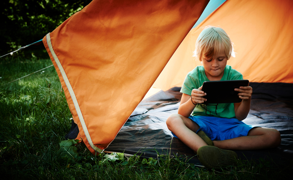 Un niño utiliza una tableta en una tienda de campaña en el campo