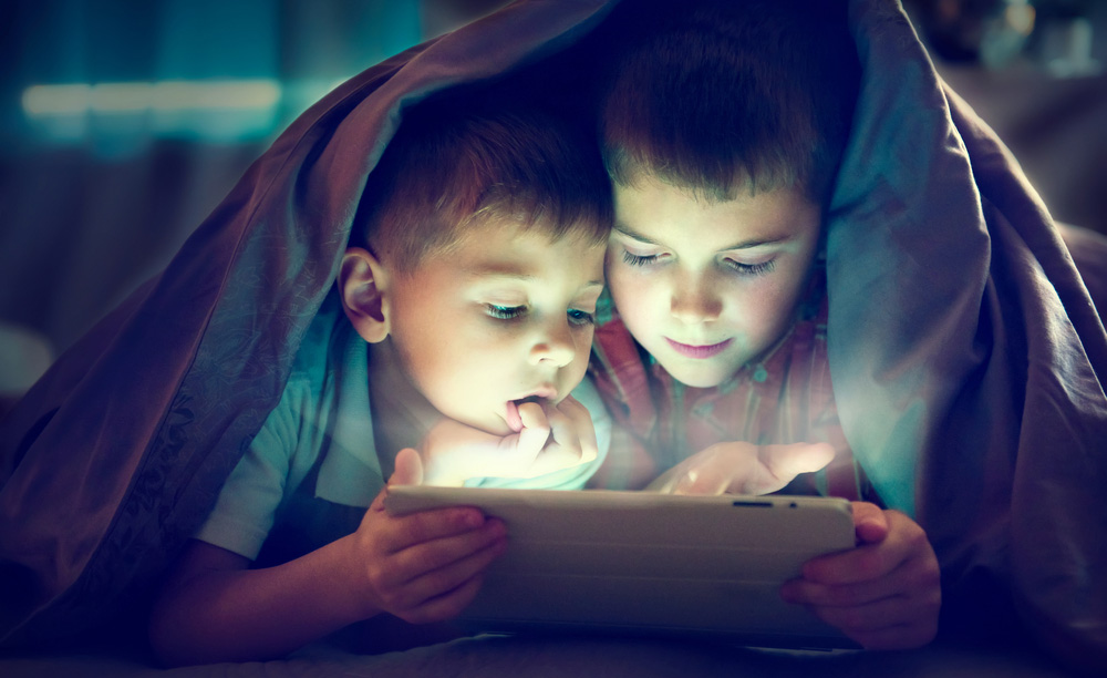 Dos niños leen un libro electrónico en una tableta en su cama