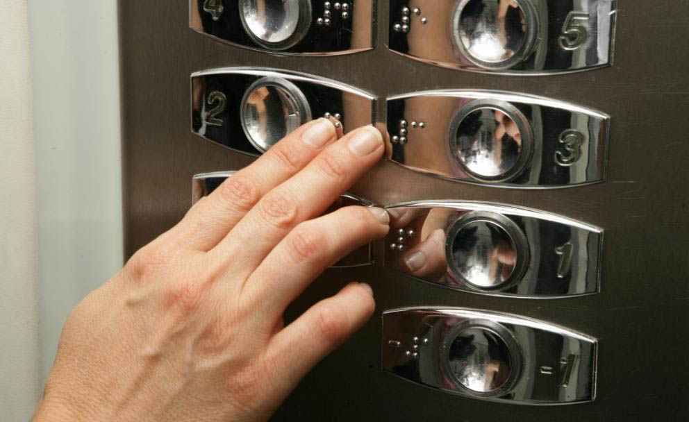 Una persona lee las indicaciones en braille en un ascensor