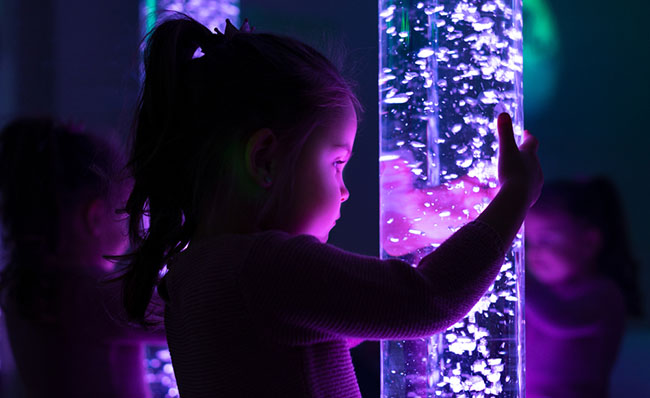 Una niña interactúa con un tubo de luces en una sala multisensorial