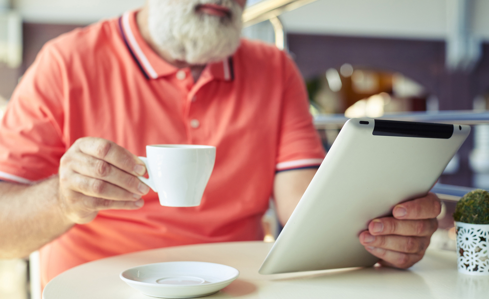 Un hombre mayor utiliza una tableta mientras toma un café