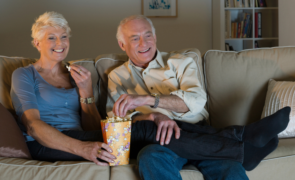 Una pareja de personas mayores sentada en un sofá viendo la televisión
