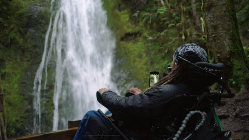 Un hombre usuarios de silla de ruedas utiliza su iPhone frente a una cascada