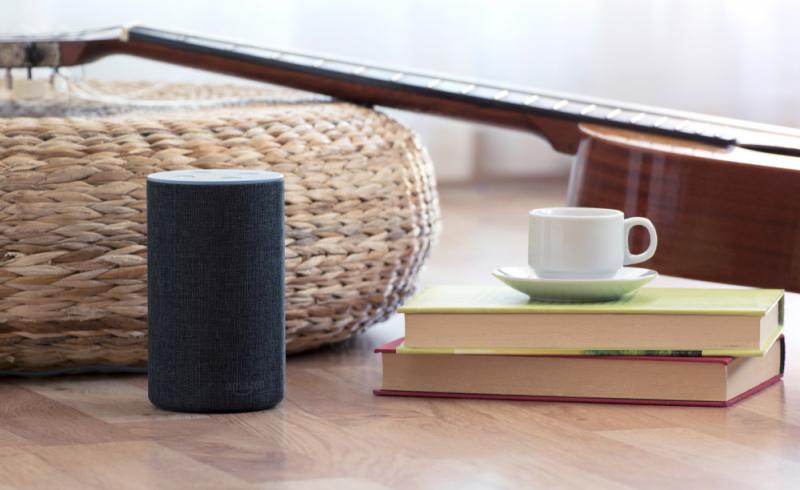 Un dispositivo Alexa de Amazon colocado sobre una mesa junto a una taza, unos libros y una guitarra