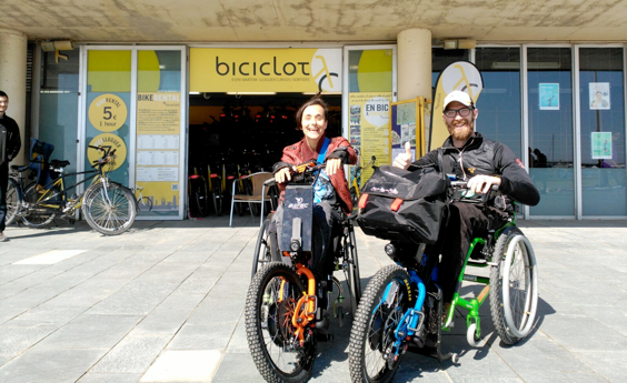 Dos turistas eslovenos utilizan las handbikes de Batec en Barcelona frente al establecimiento de Biciclot