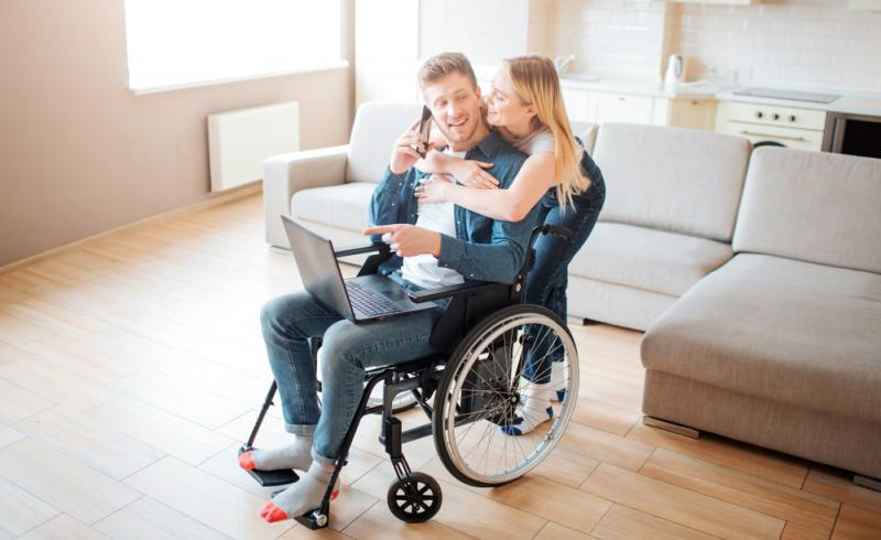 Un hombre en silla de ruedas y una mujer utilizan un ordenador en su nueva casa