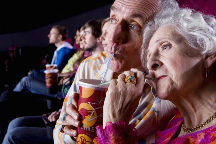 Una pareja de personas mayores beben un refresco en un cine