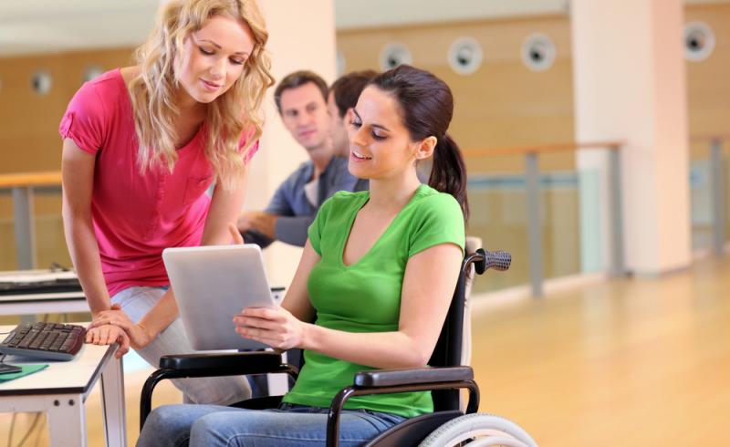 Una joven con discapacidad física utiliza una tableta junto a otra estudiante