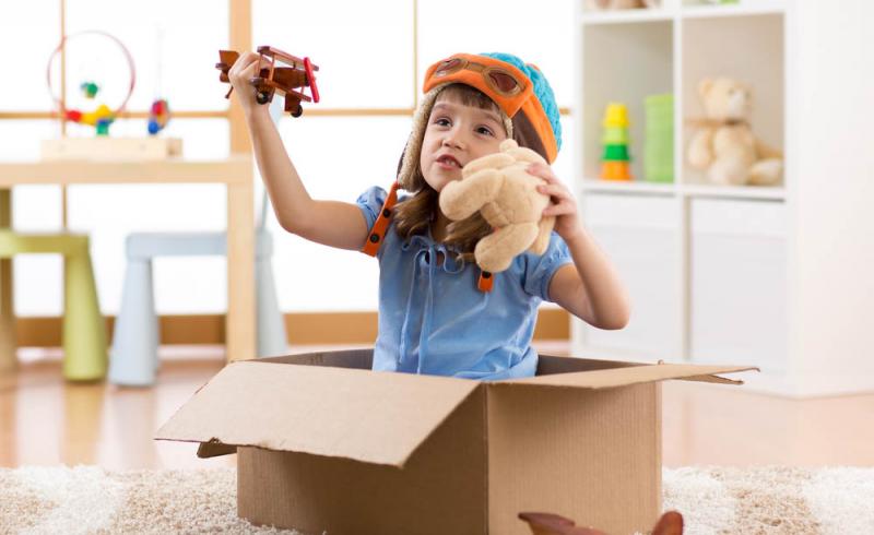Una niña juega con varios juguetes dentro de una caja de cartón