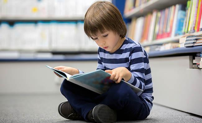 Un niño lee un cuento sentado en el suelo de una biblioteca